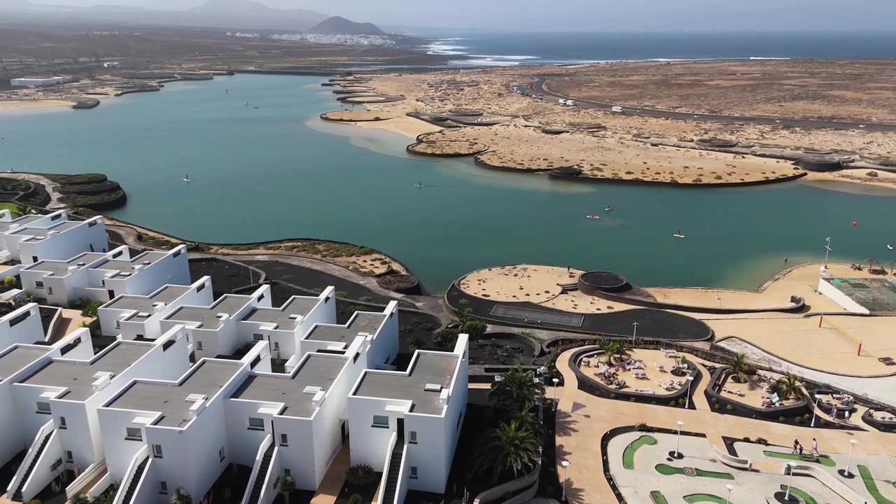 Edifici bianchi di un resort si affacciano su una laguna, aree ricreative e una costa arida, ripresa aerea orbitale a mezzogiorno.