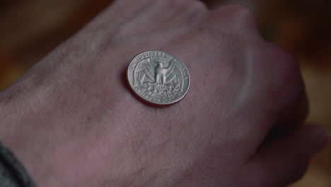 el hombre muestra una moneda de un cuarto de dólar en el dorso de la mano con el puño