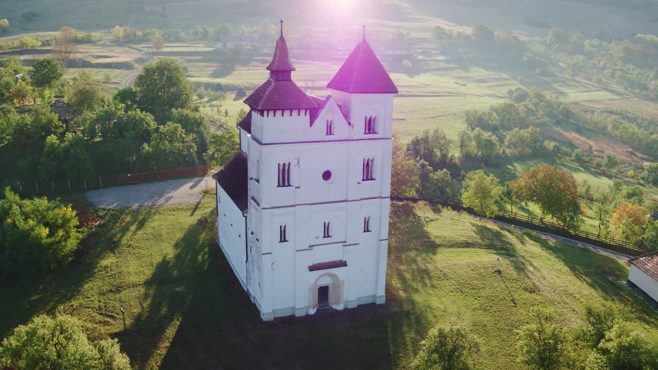 Drone dari gereja putih bersejarah di Herina, Bistrita Nasaud, Rumania, dengan atap merah, di lembah pagi yang tenang dan berkabut