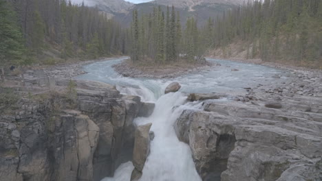 A-picturesque-waterfall-surrounded-by-a-lush-forest-and-mountains