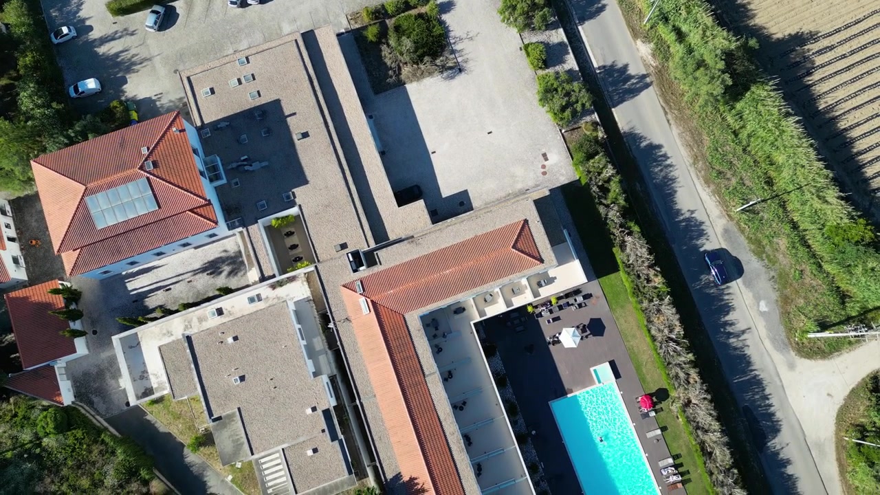 Luftfoto af et hotel og dets parkeringsplads omgivet af frodige grønne områder i Portugal, der viser en harmonisk blanding af natur og arkitektur
