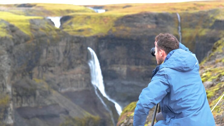 Fotografo con giacca blu che immortala l'ipnotica cascata Haifoss da un punto di osservazione impervio, Islanda.