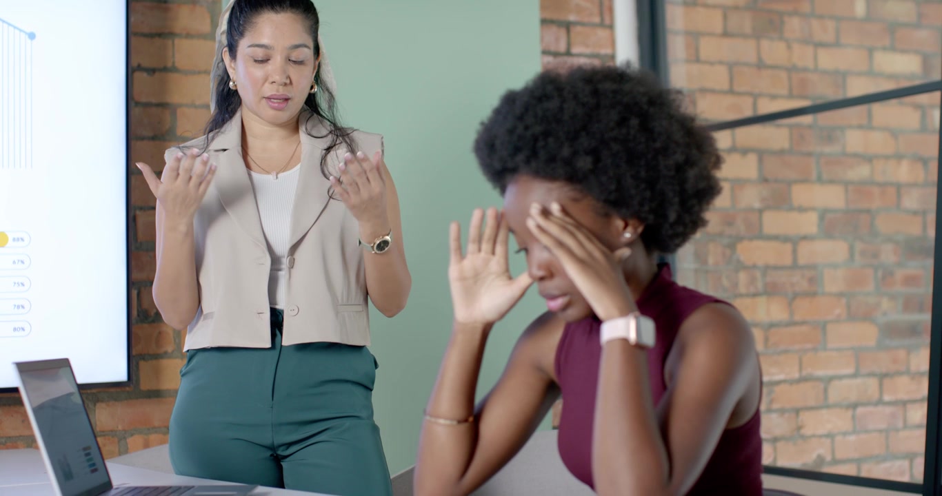 Diverse female coworkers in meeting, presenter explaining chart, woman rubbing temples, copy space