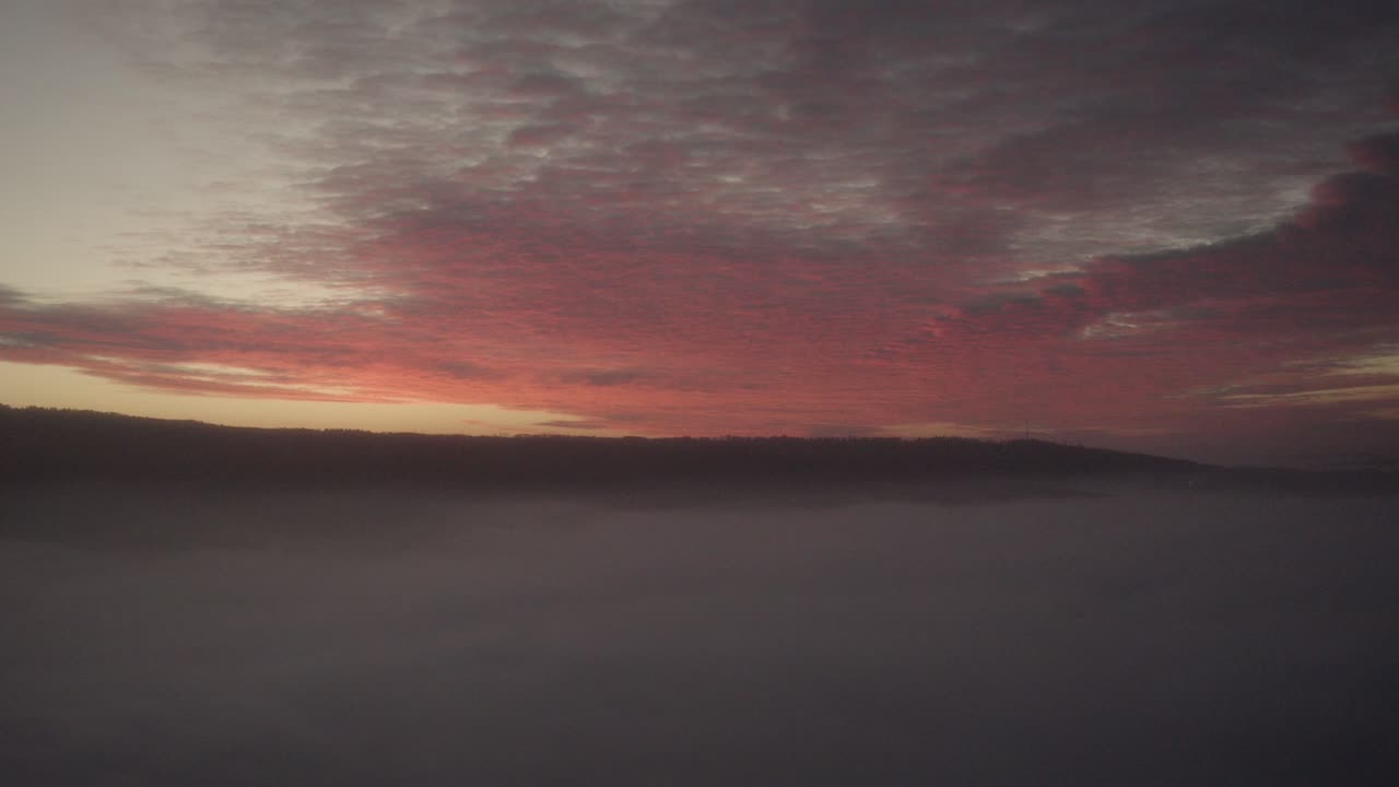 Aerial of the most amazing play of light at sundown: Red and orange sunset over fog mist