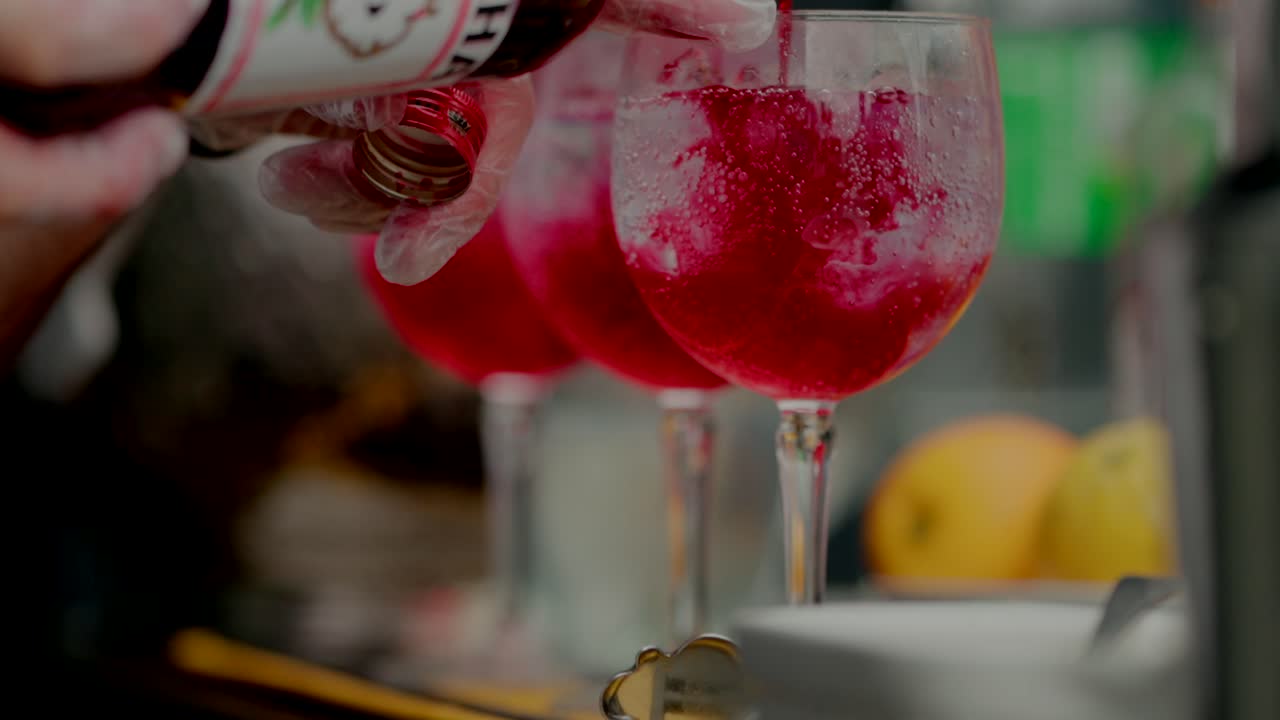 Gloved hands preparing red cocktails with fruit garnish in transparent glasses