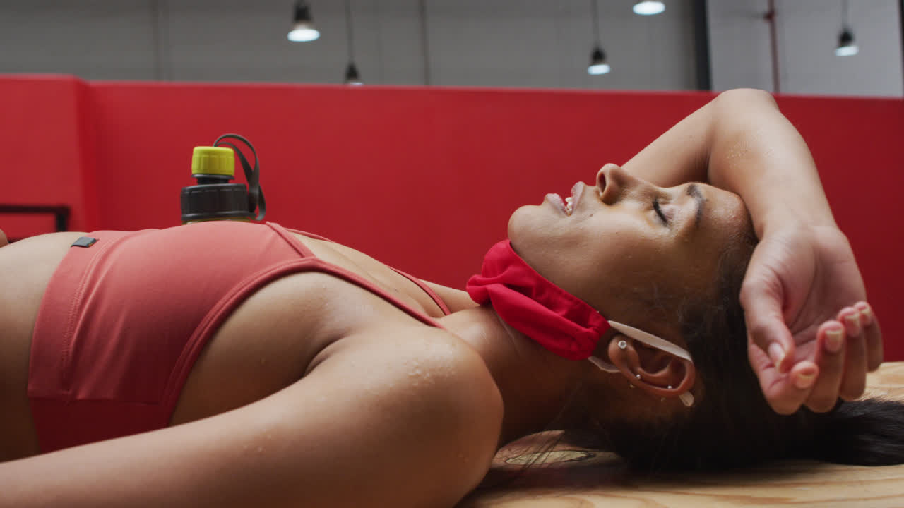 Donna caucasica in forma con mascherina al collo sdraiata su plyo box in legno in palestra