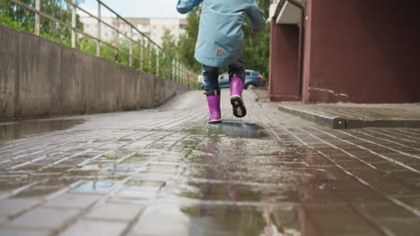 una niña con botas púrpuras saltando en un charco en un día de lluvia