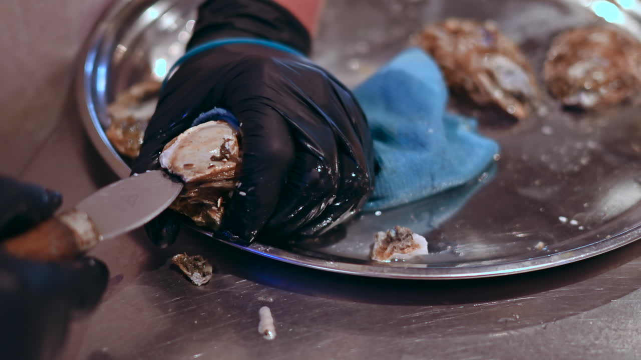 Man hands cleaning and opening oysters with special knife at seafood restaurant, slow motion