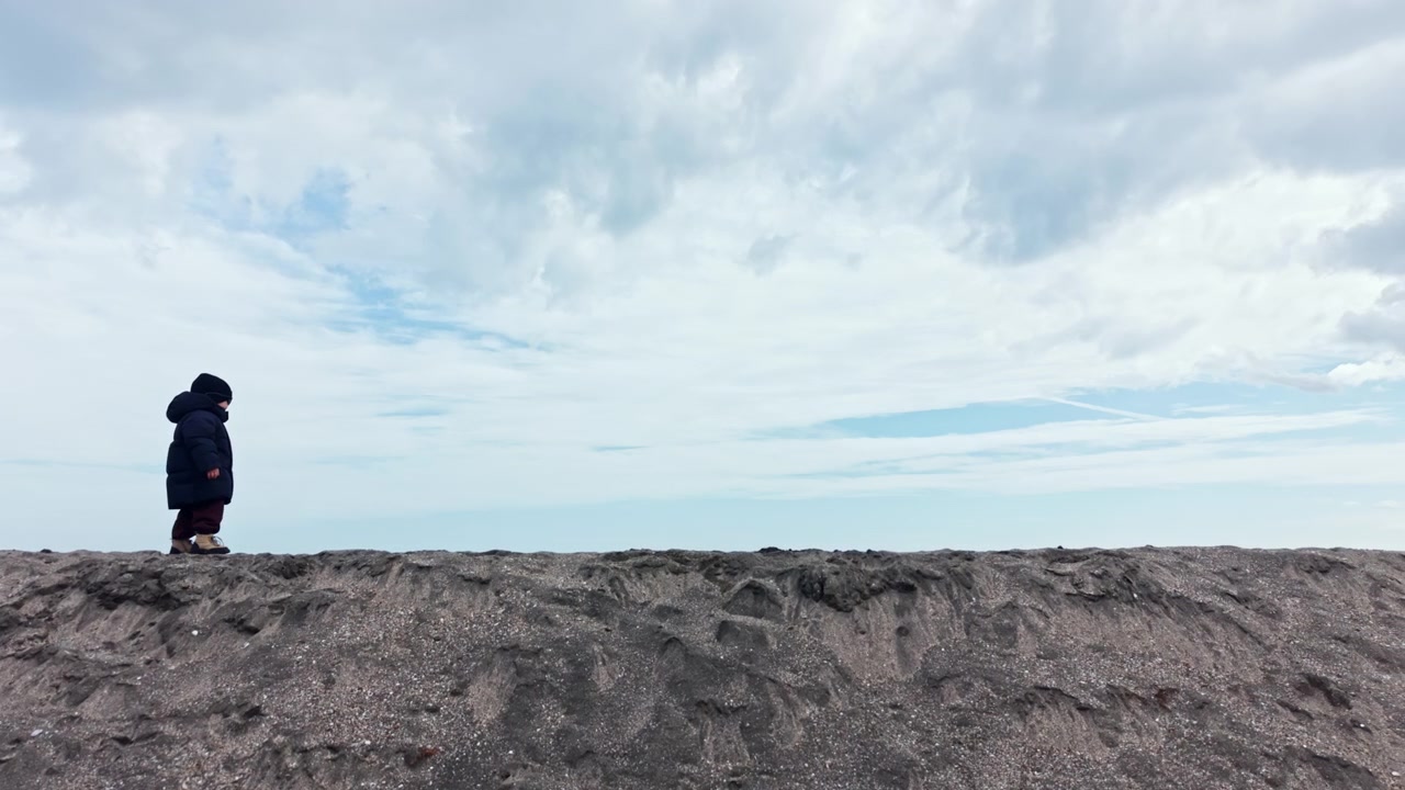 涼しい日、曇り空の下、水辺の近くの砂浜を歩く子供。