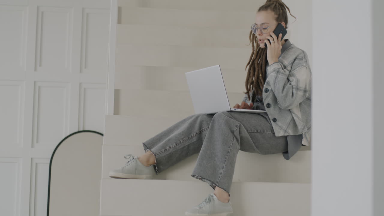 Woman working on laptop and talking on the phone on stairs