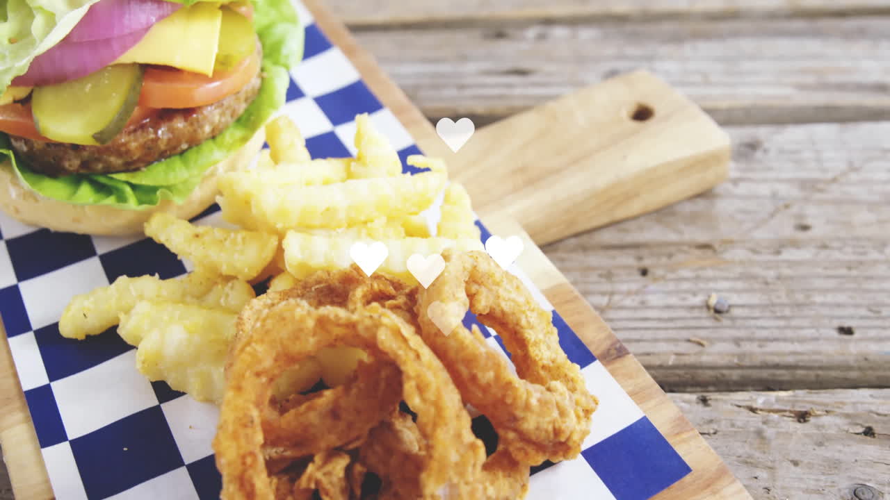 Burger with lettuce, tomato, fries, and onion rings on checkered paper