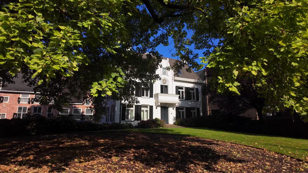 Shadowed townhouse facade glimpsed through leafy green branches on a sunny day in Coevorden. Location: Coevorden, Drenthe, Netherlands Coevorden, Drenthe, Nederland