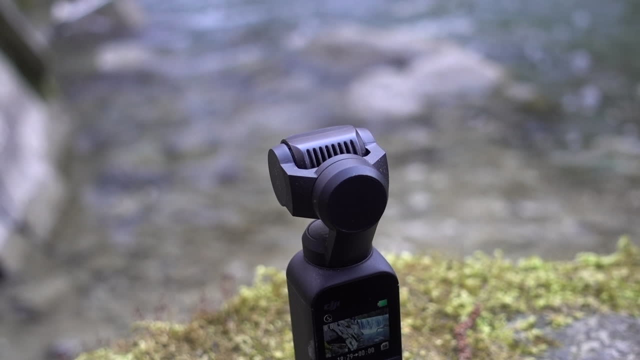 dji osmo 포켓 카메라는 스위스 알프스의 강 가장자리에 있는 이끼 지지대에 놓여 있습니다.