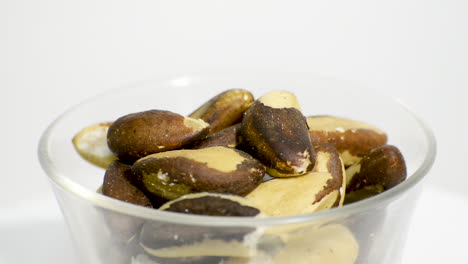 transparent glass bowl with brazil nuts rotating on a white background