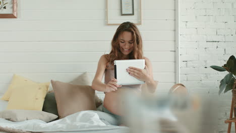 mujer embarazada hablando en una cama de video chat. madre embarazada con una tableta en casa