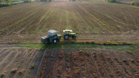 aerial: side follow of a tractor with trailer in an empty field