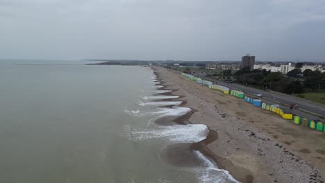 overcast day on a uk pebble beach. gentle waves wash the textured shore. colorful beach huts line the beach next to a road with cars.