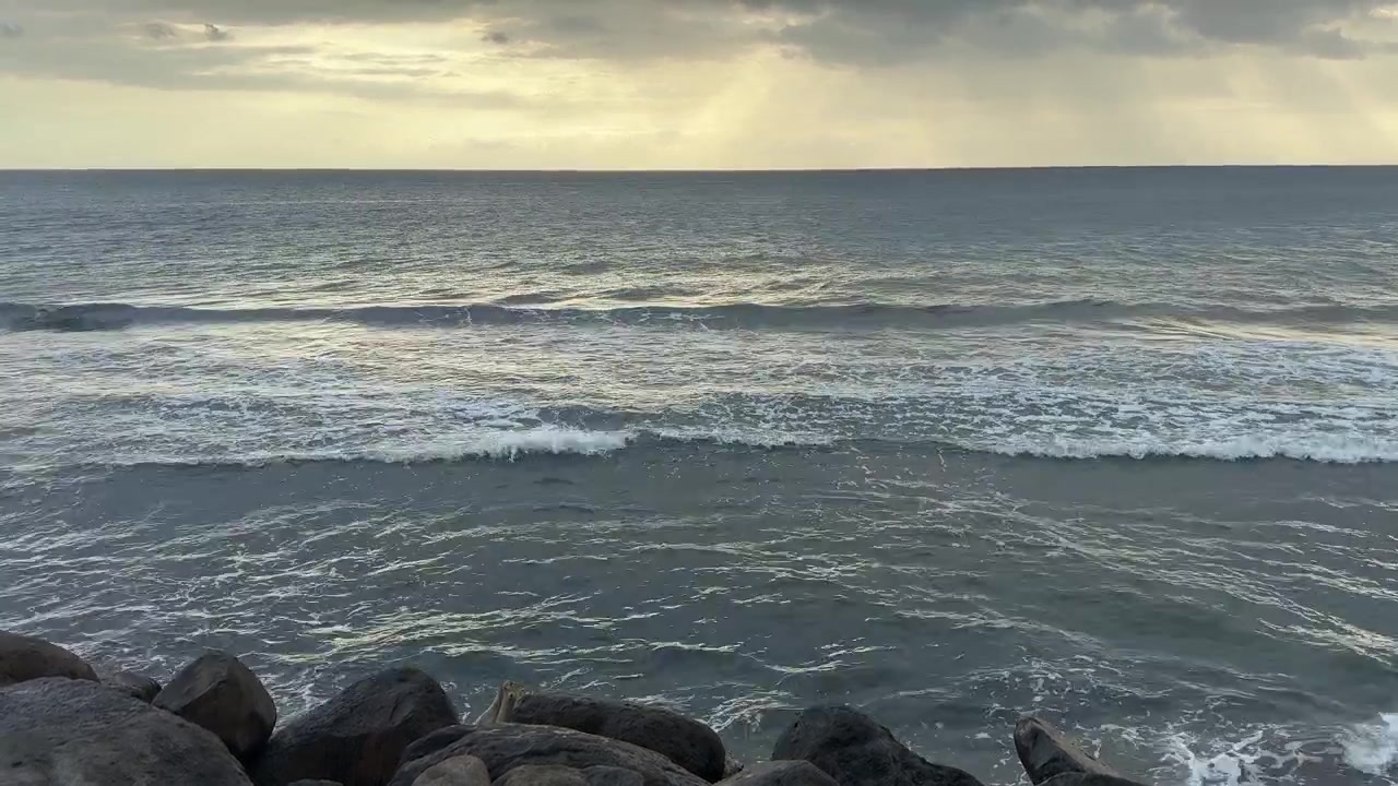 Onde oceaniche che si infrangono su una costa rocciosa con raggi di sole che filtrano tra le nuvole.