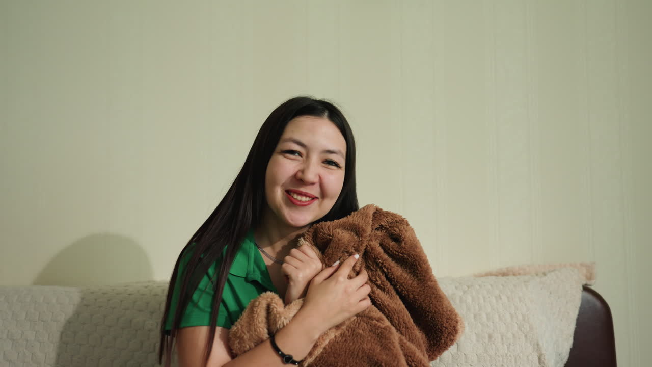 Donna rilassata che si riposa con una morbida coperta all'interno, donna asiatica rilassata avvolta in una soffice coperta a casa, donna serena che si gode un momento di pace avvolta in un caldo plaid sul divano del soggiorno