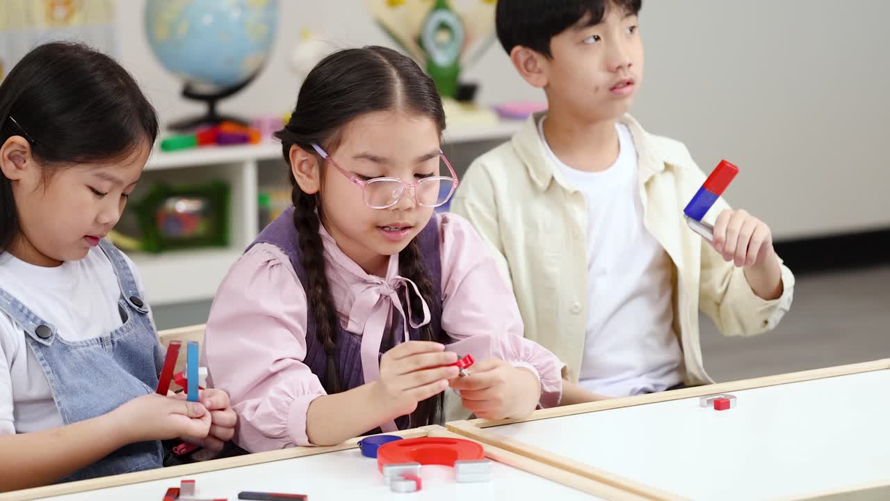 明るい教室で、小学生の生徒3人が棒磁石を使って磁力を調べています。