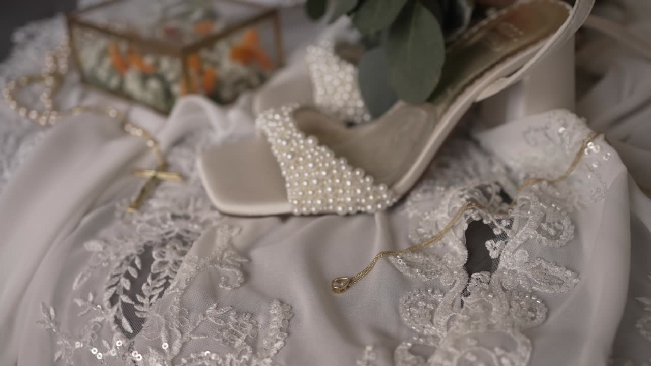 Close up of pearl bridal heels on white lace fabric with gold jewelry and floral decor