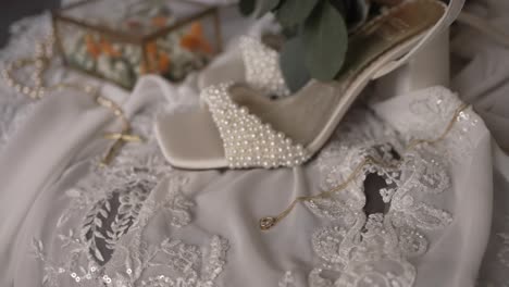 close up of pearl bridal heels on white lace fabric with gold jewelry and floral decor