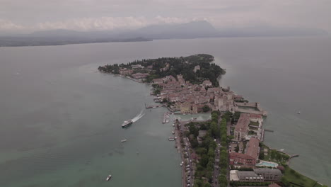 Toma-De-Drone-De-Simione-Italia-Mirando-La-Antigua-Fortaleza-En-Un-Día-Gris-Con-Barcos-En-El-Agua-Cerca-Del-Lago