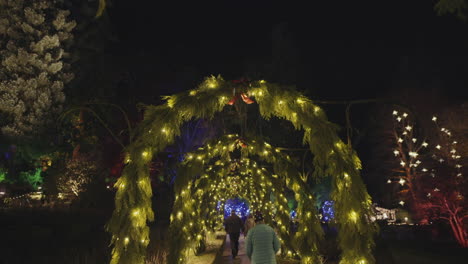 wide steadicam shot of walkway decorated with christmas lights and arches, night