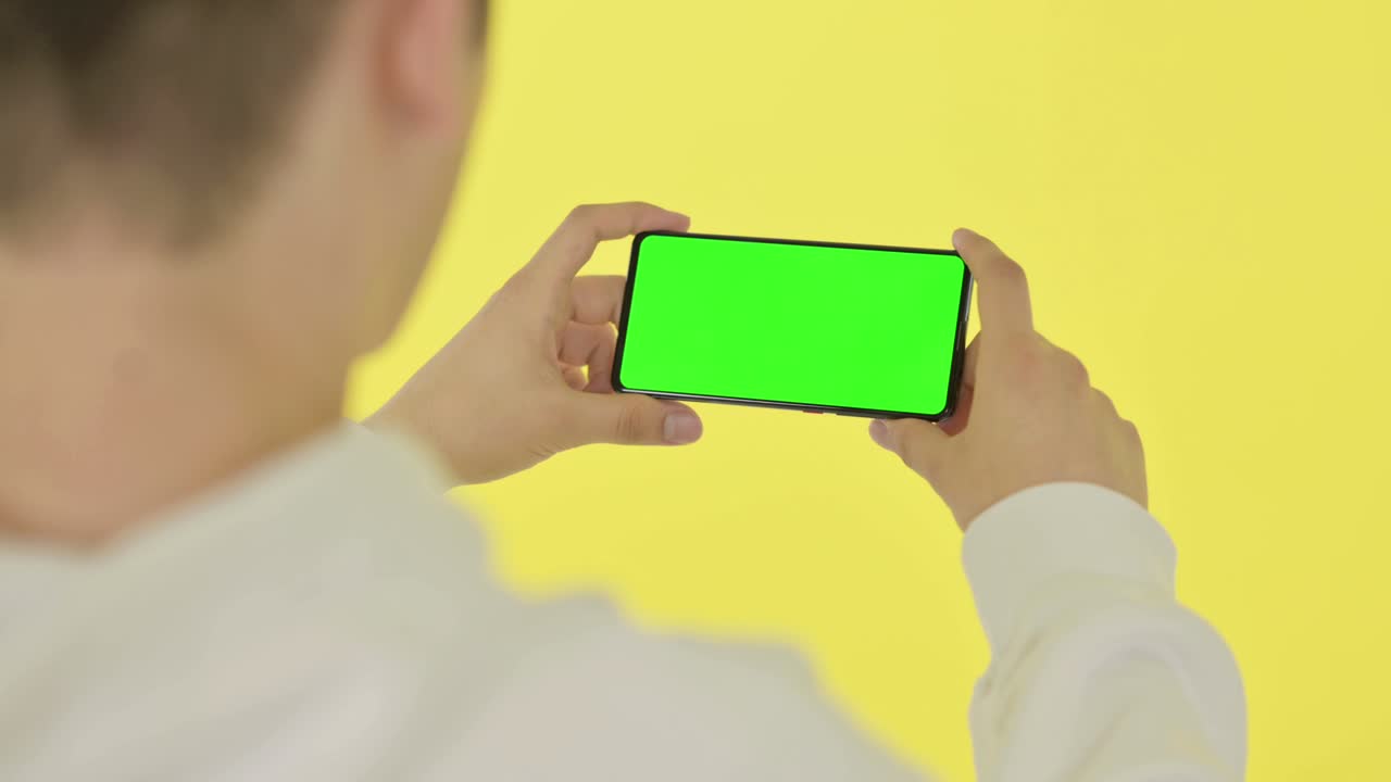 초록색 화면, 노란색 배경으로 수평 스마트폰을 보는