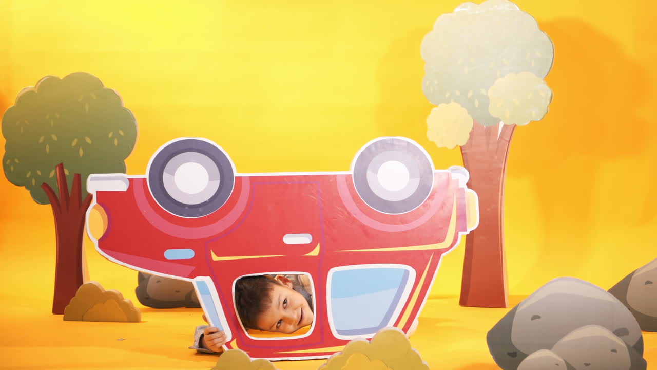 Little boy with a red car in the studio. Yellow background. Bright scenery.