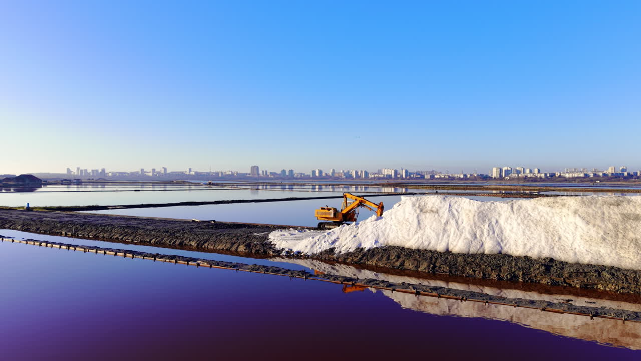 Ampia veduta aerea di un paesaggio con diverse vasche di evaporazione del sale con acqua rosa e viola. Cumuli di sale bianco sono disposti lungo argini industriali.