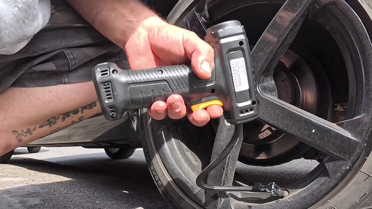 Man holding rechargeable portable air pump to inflate van tyre and checking the pressure