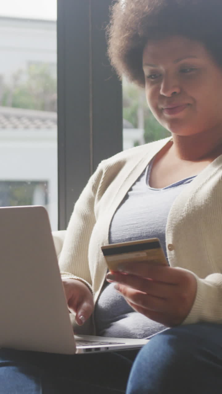 video de una feliz mujer afroamericana de tamaño plus con tarjeta de crédito y usando una computadora portátil