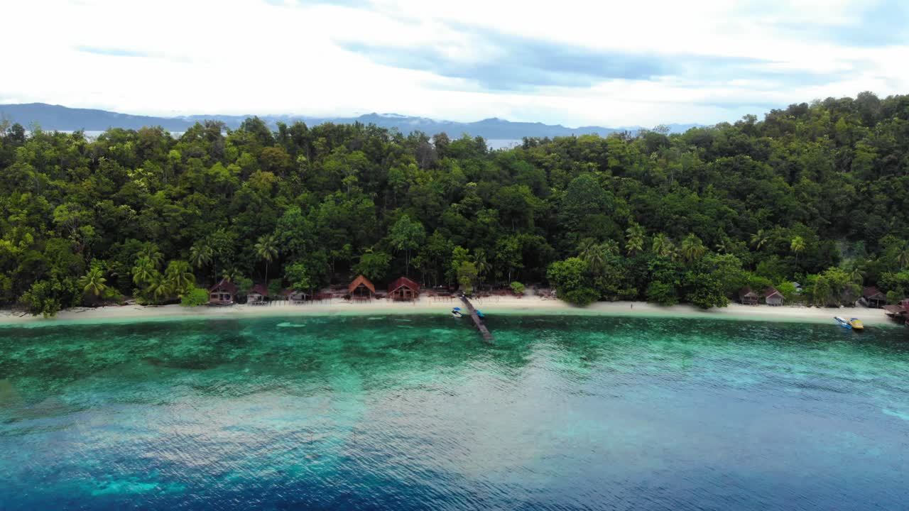 Aerial View of a Tropical Island Beach with Bungalows, Pier, and Clear Blue Water