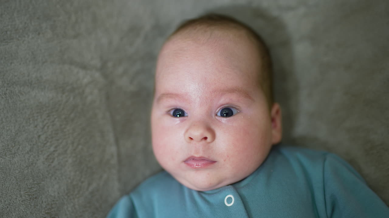 Little baby watching intensely into the camera. Cute child on the grey background. Close up.