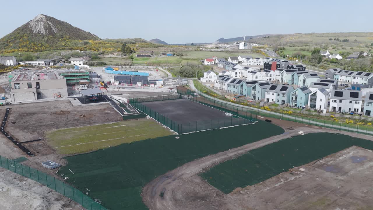 Aerial sweep of new Cornish suburb under construction with neat rows of scaffolded houses, fresh roads and earthworks illustrating rapid master-planned residential development