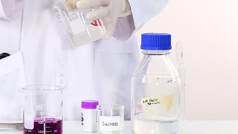 a scientist pours liquid into a beaker beside a sucrose container and a labeled bottle.