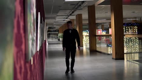 Young-blonde-man-in-a-black-suit-with-bow-tie-walking-in-the-art-gallery-to-the-auction.-Slow-Motion