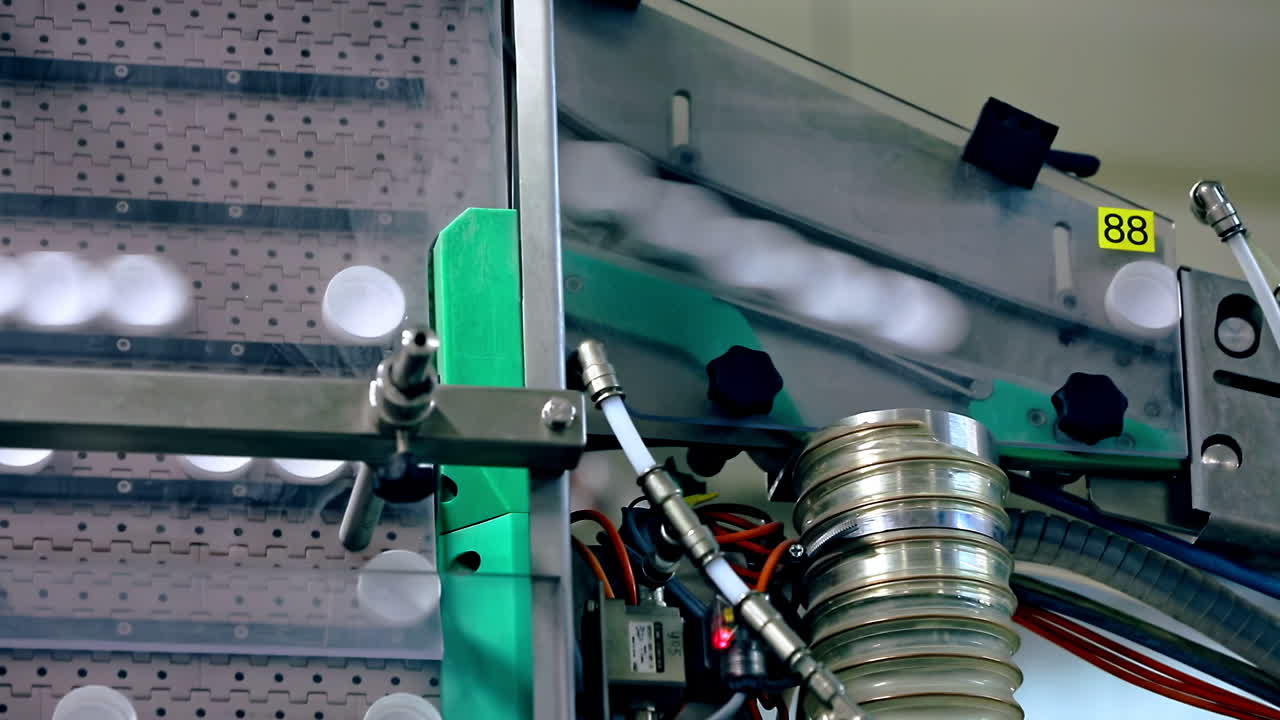 Industrial production line with automated machinery manufacturing with white plastic bottle caps falling from conveyor belt at factory, exhibition. recycling, industry, technology equipment concept