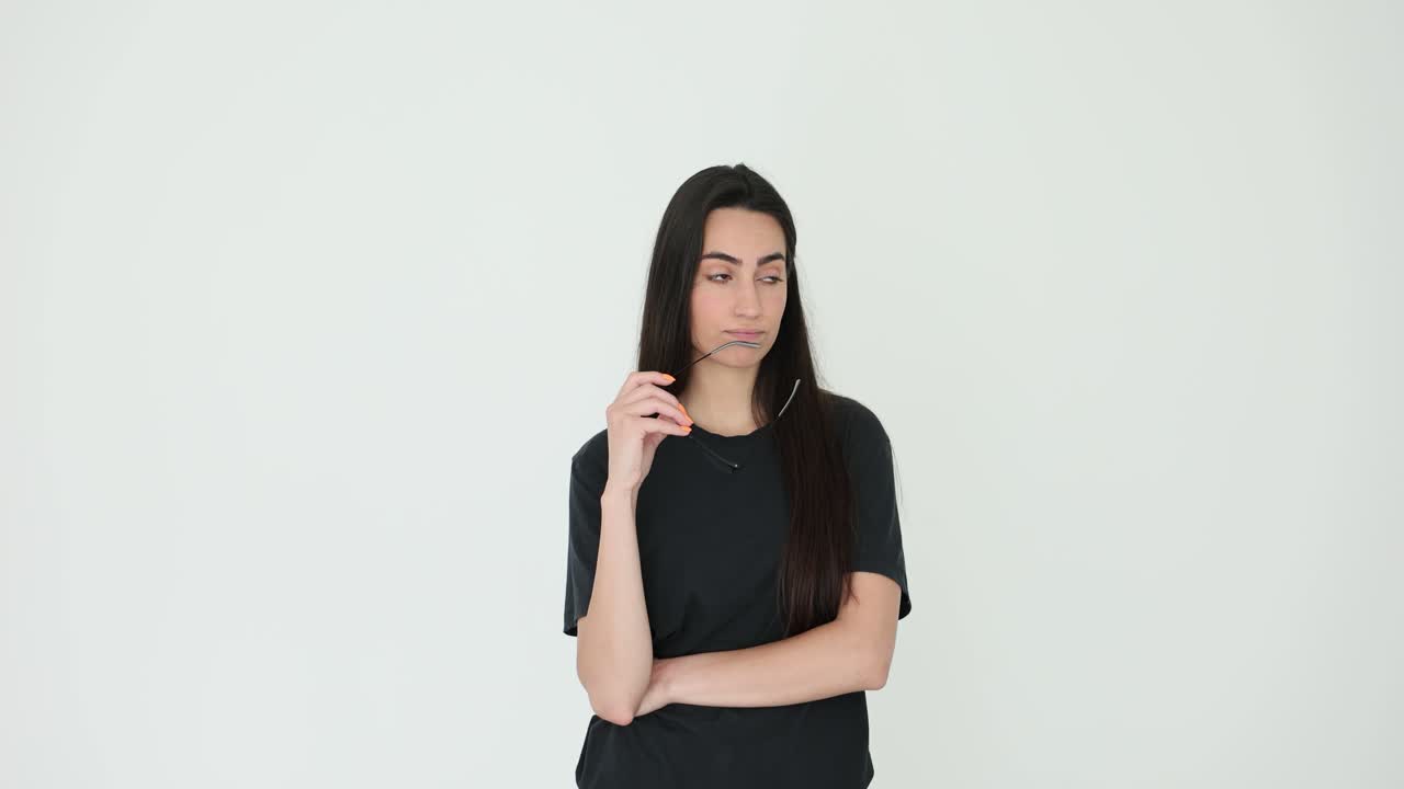 Thoughtful Young Woman Holding Glasses Against a White Background
