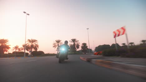 Una-Toma-De-Una-Motocicleta-Negra-Dando-Vueltas-Alrededor-De-Una-Rotonda-En-Una-Escena-De-Persecución,-Un-Motociclista-Vestido-De-Negro-Paseando-Por-Abu-Dhabi-Durante-Una-Puesta-De-Sol-épica