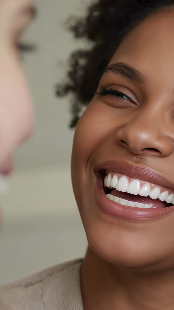 Vertical video: Smiling woman widening smile as friend speaking in room, stud earring, beige top