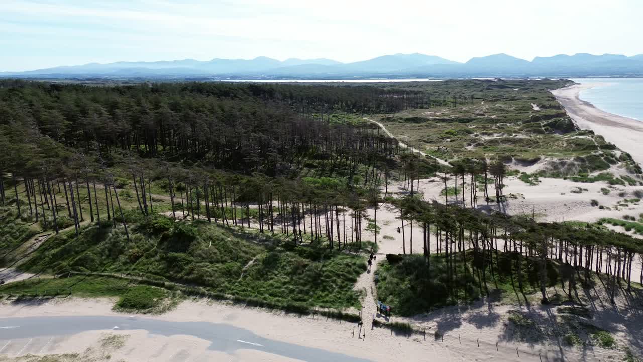 Newborough forest aerial panning view sunny woodland car park coastline and Snowdonia mountain range
