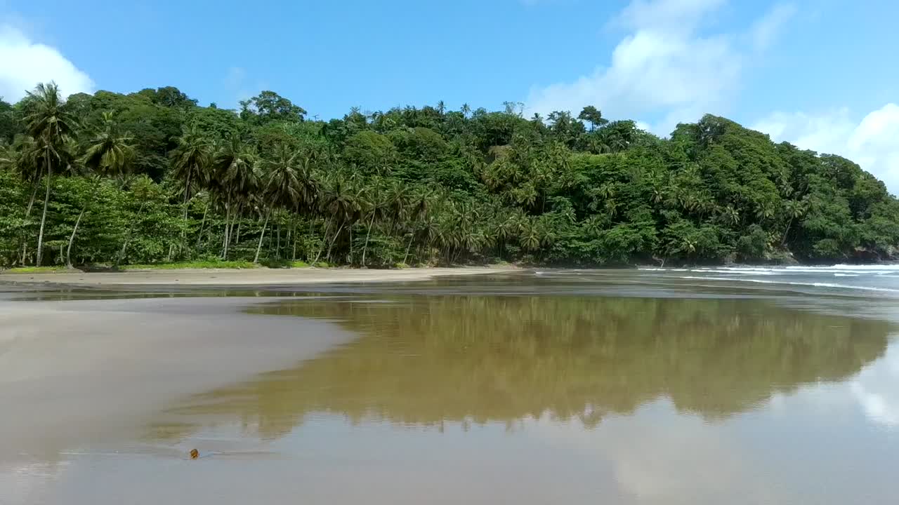 aéreo a lo largo de una playa vacía de arena negra con efecto espejo, isla de são tomé