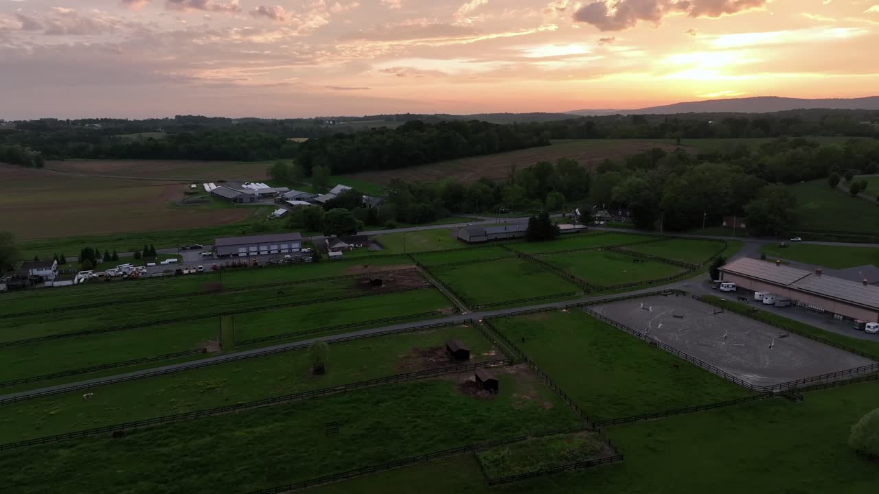 Traffic on rural interstate road near farmstead and industrial Companies in american countryside. Golden sunset at horizon. Aerial wide shot. Green cropland farm fields in United States at dusk.