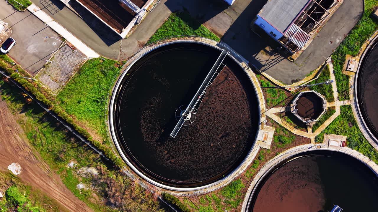 A circular settling tank with rotating scraper bridge and dark water. Aerial view of primary clarifier tank in sewage plant
