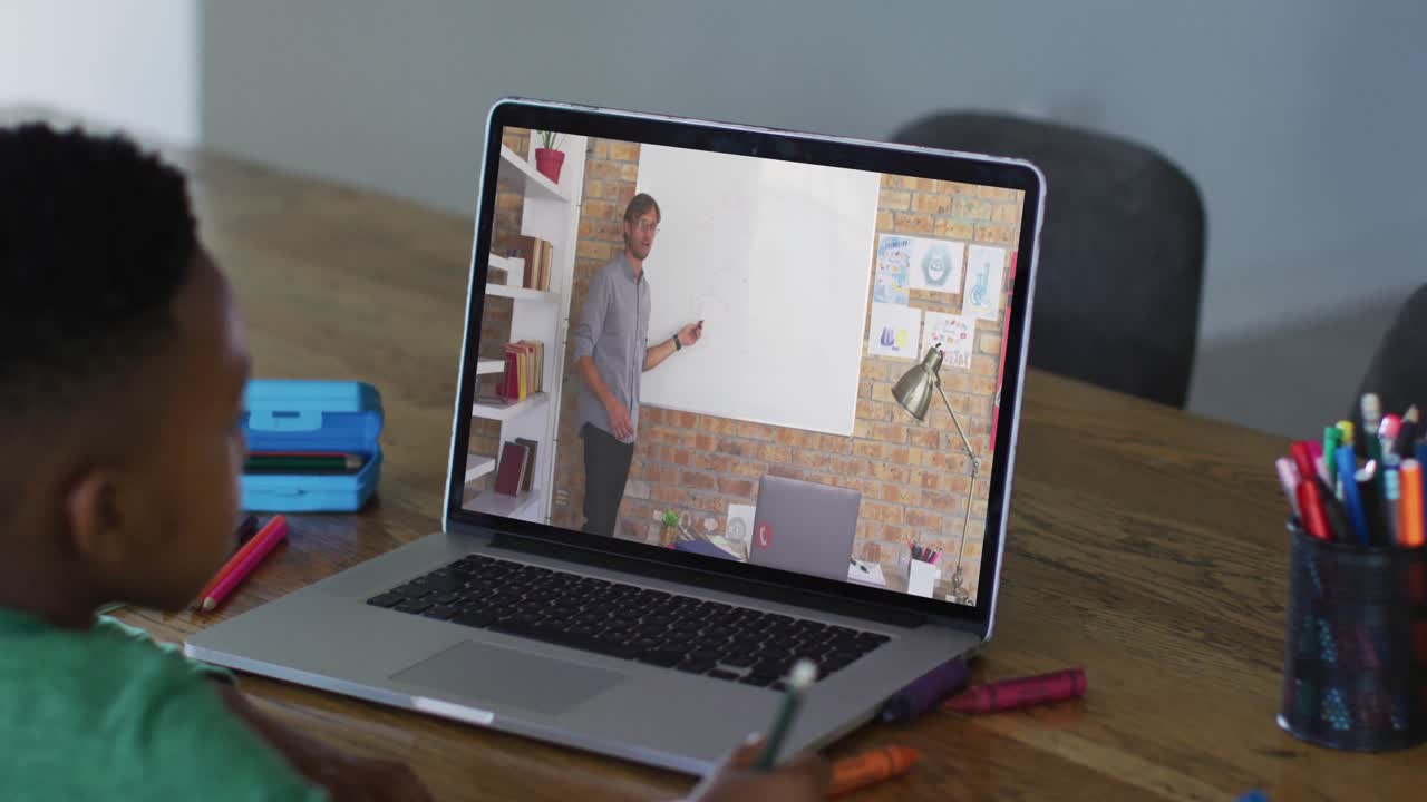 niño afroamericano haciendo la tarea mientras tiene una videollamada con un profesor masculino en una computadora portátil en casa