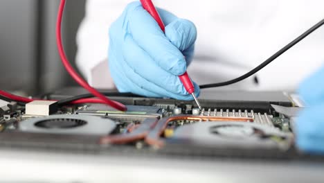 technician diagnosing laptop motherboard with multimeter
