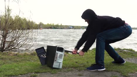 angry man destroying a computer by the lake