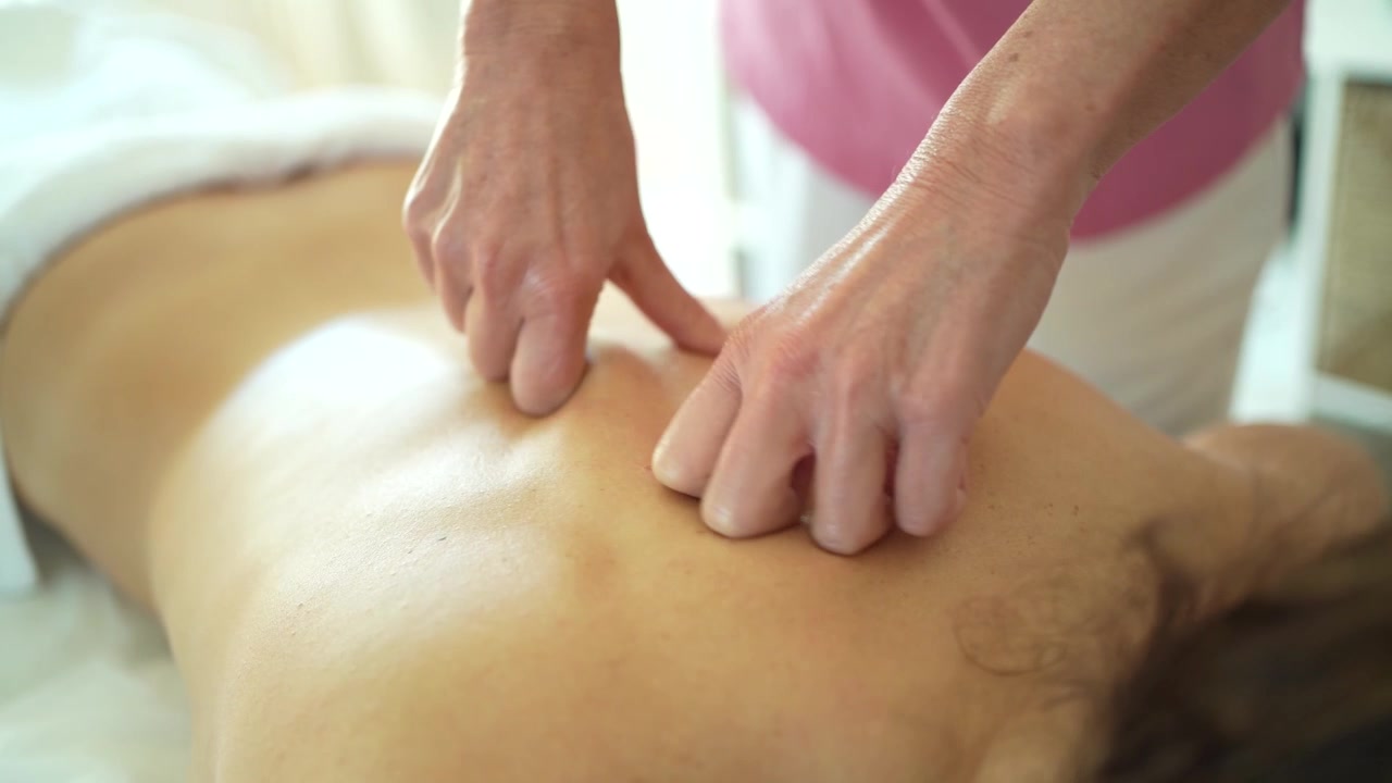 Osteopat masserer ryggen med hænder på klinik.